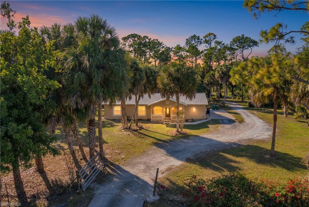 1867 17th Street Southwest Naples, FL 34117 - Photo 28 of 31 View of front of home with dirt driveway, a porch, a yard, stucco siding, and view of scattered trees