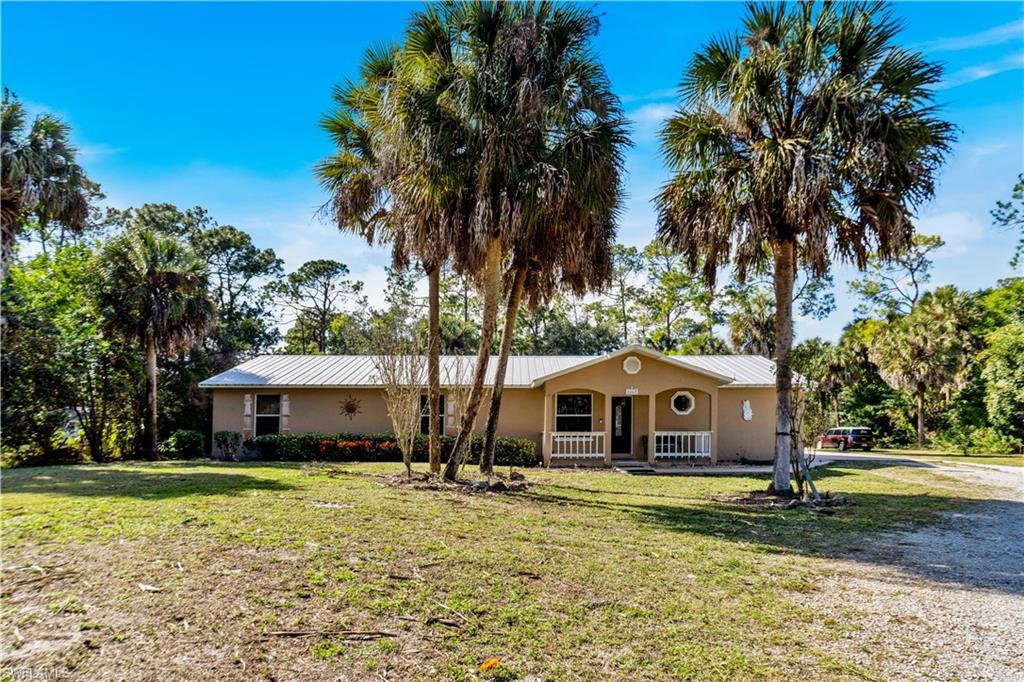 1867 17th Street Southwest Naples, FL 34117 - Photo 4 of 31 View of front facade featuring a porch, a front lawn, stucco siding, a metal roof, and driveway