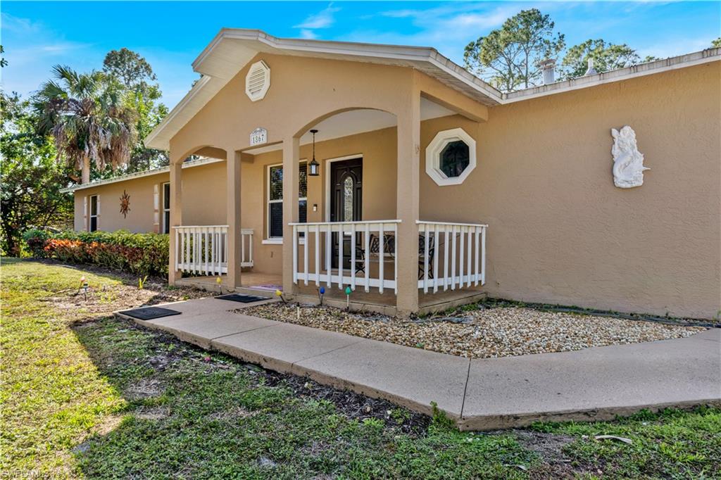 1867 17th Street Southwest Naples, FL 34117 - Photo 5 of 31 Property entrance featuring covered porch, stucco siding, and a yard