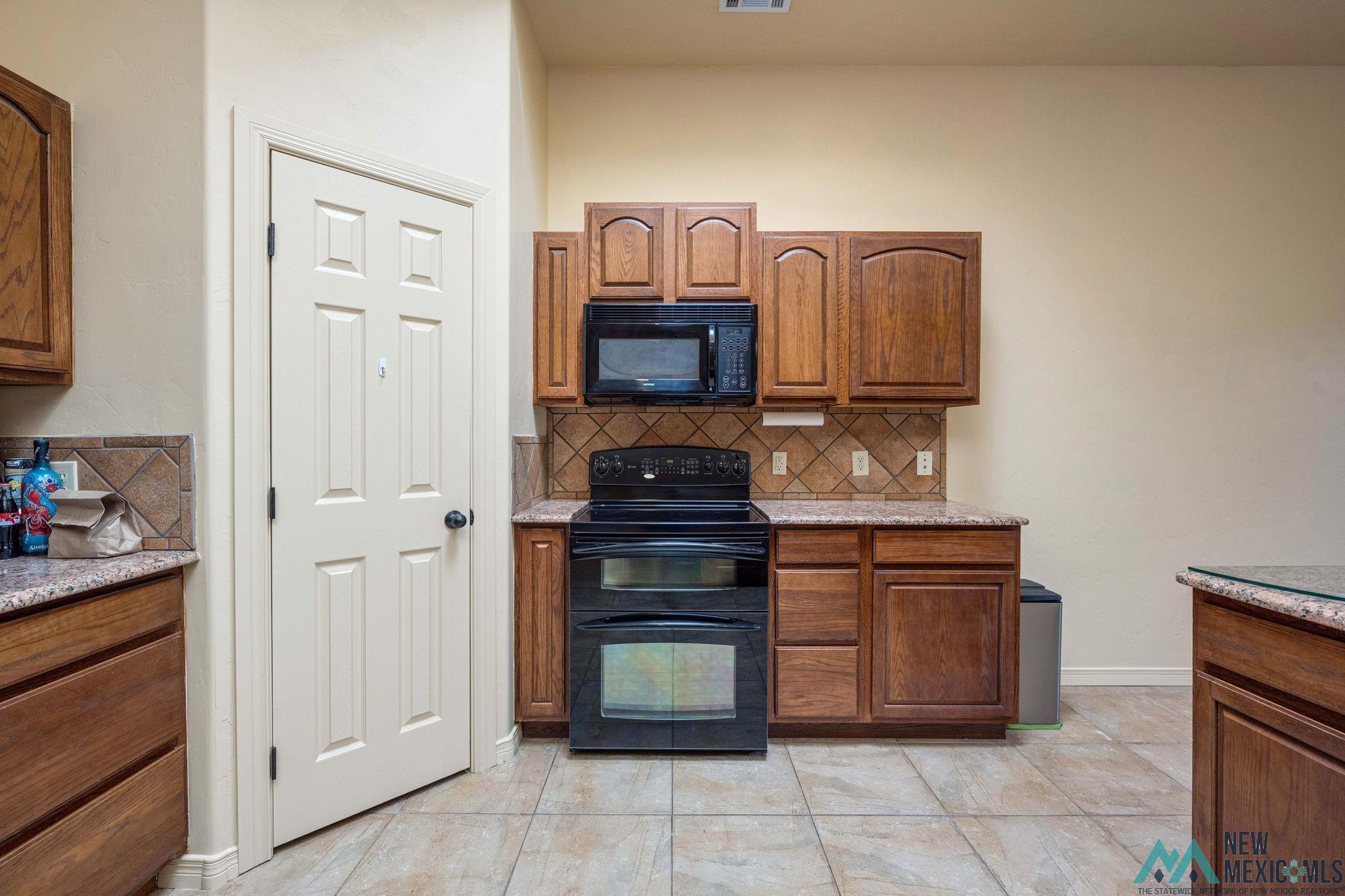 3884 Adriatic Road Las Cruces, NM 88012 - Photo 17 of 45 Kitchen featuring wood cabinetry, solid surface countertops, tile flooring, and a tile backsplash