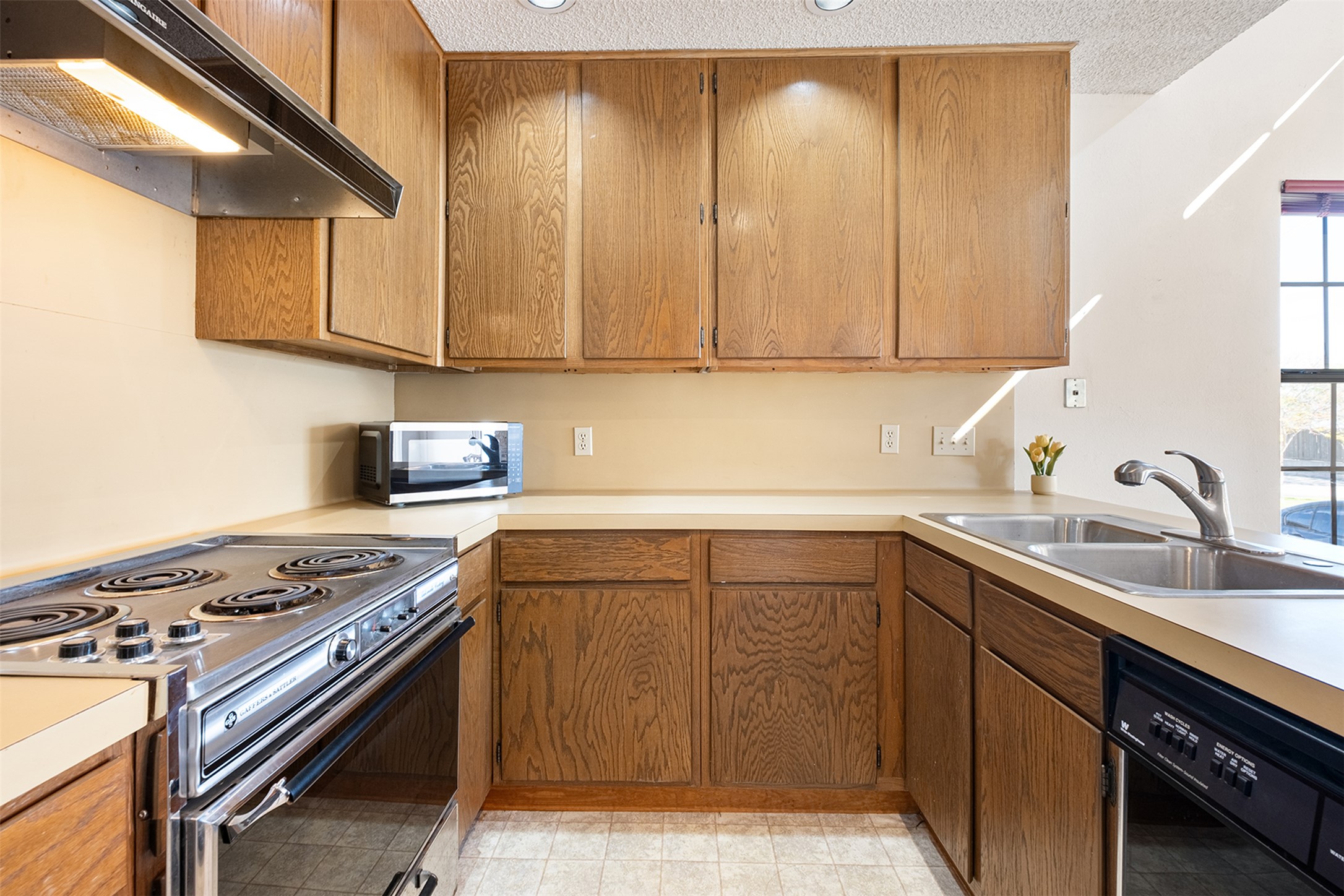 1748 Ohlen Road, Unit 16 Austin, TX 78757 - Photo 15 of 38 Kitchen featuring range hood, stainless steel appliances, light countertops, wood finish cabinetry, and a textured ceiling