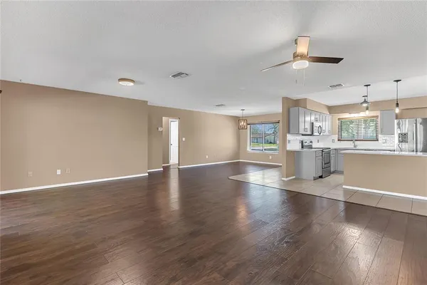 an empty room with wooden floor kitchen view and a window