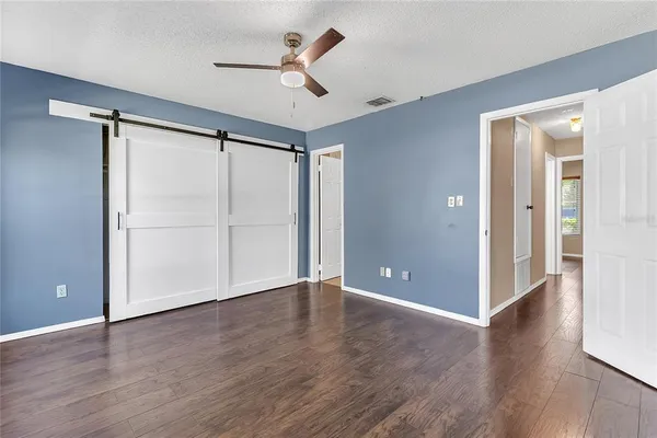 a view of an empty room with wooden floor and a ceiling fan