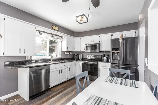 a kitchen with stainless steel appliances granite countertop a stove top oven a sink dishwasher a refrigerator and white cabinets with wooden floor
