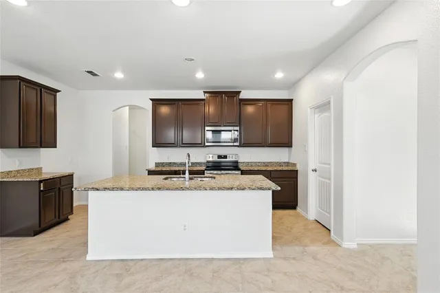 a large kitchen with stainless steel appliances granite countertop a stove a sink a refrigerator and a granite counter tops with wooden cabinets