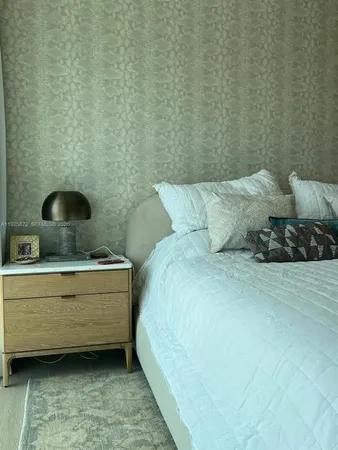 a bedroom with a bed a chair and a large window with the balcony view