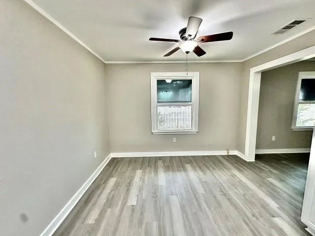 an empty room with wooden floor chandelier fan and windows