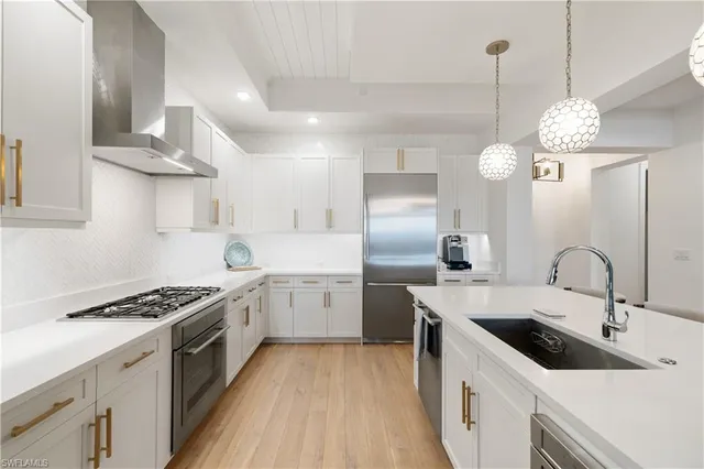 a kitchen with stainless steel appliances a sink a stove a kitchen island with wooden floor and cabinets