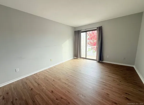 a view of an empty room with wooden floor and window
