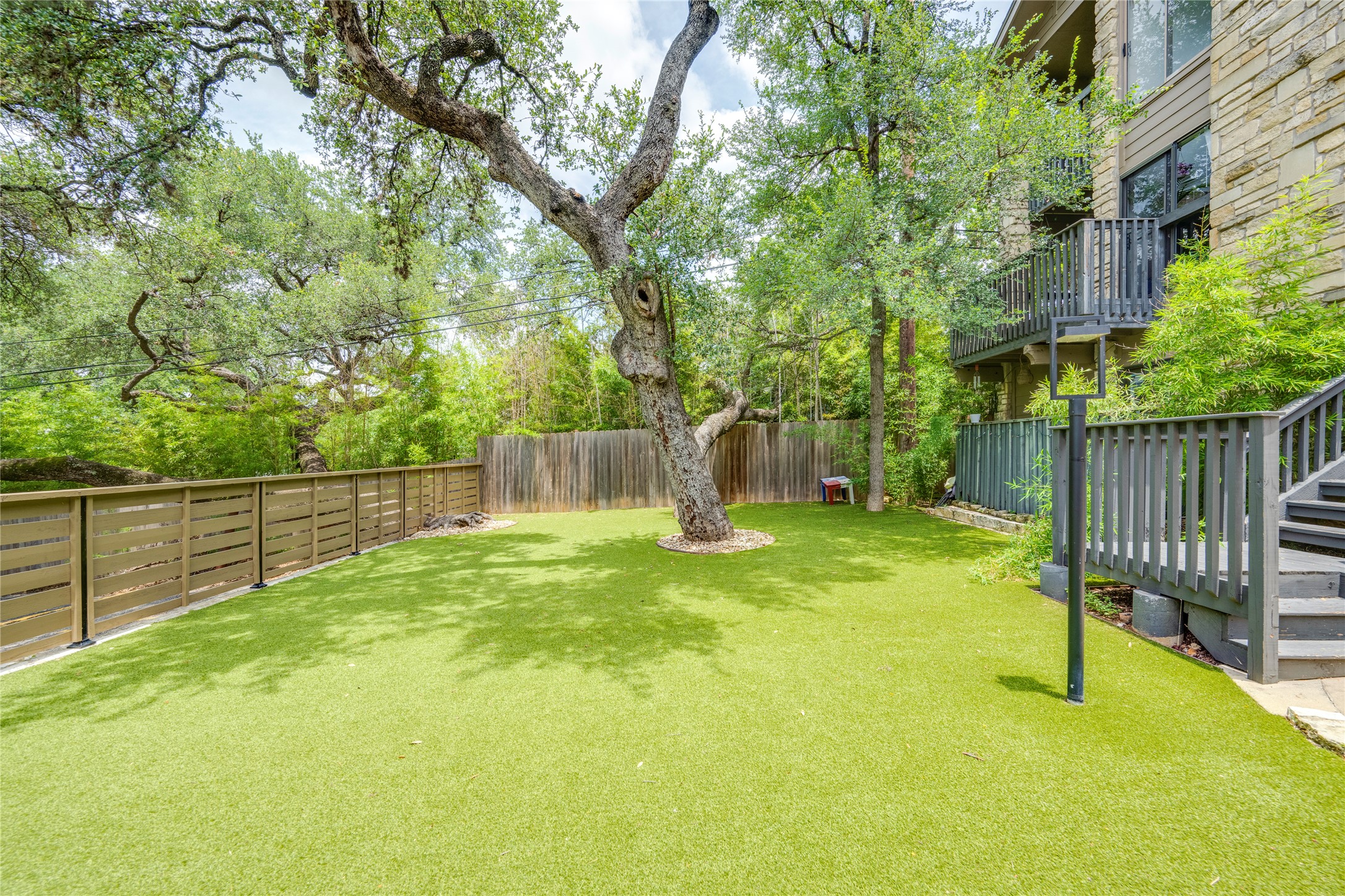 3627 Menchaca Road, Unit 214 Austin, TX 78704 - Photo 23 of 28 A verdant backyard with artificial turf and mature trees, featuring a modern exterior with multiple balconies and privacy fencing.