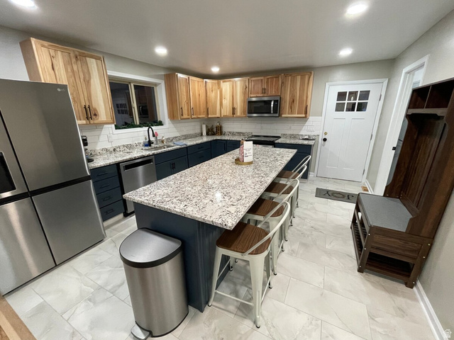 2807 North Ogden Canyon Road Eden, UT 84310 - Photo 12 of 72 Modern kitchen featuring a large island with a light-toned countertop, a stainless steel refrigerator, dark blue base cabinetry, natural wood-finish upper cabinetry, and light-toned tile flooring