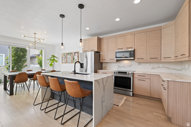 947 West Cushing Road Riverton, UT 84065 - Photo 1 of 1 Kitchen featuring light stone countertops, stainless steel appliances, an island with sink, a kitchen breakfast bar, and light wood finished floors