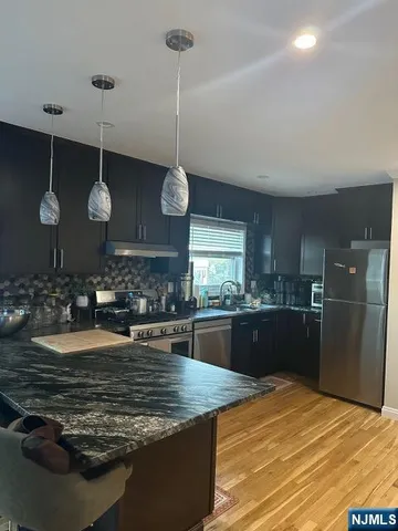 a kitchen with stainless steel appliances granite countertop a sink a stove top oven a clock and cabinets