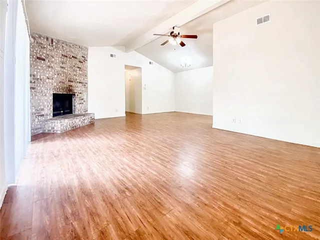 a view of an empty room with wooden floor and a fireplace