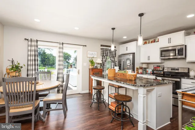 a kitchen with stainless steel appliances granite countertop a stove top oven a refrigerator a dining table and chairs with wooden floor