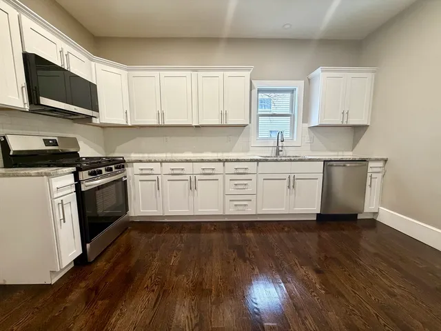 a kitchen with granite countertop wooden floors stainless steel appliances and white cabinets