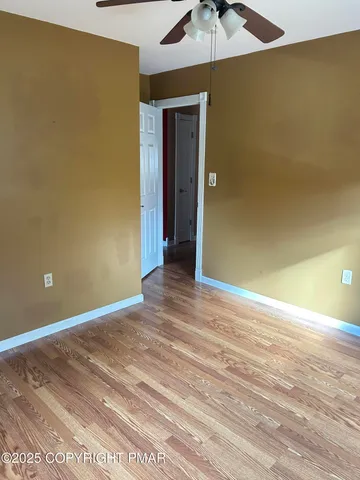 an empty room with a chandelier fan and wooden floor