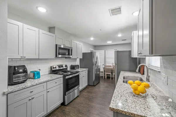 a kitchen with stainless steel appliances granite countertop a stove a sink a refrigerator and white cabinets