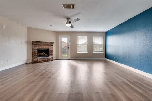 an empty room with wooden floor fireplace and windows