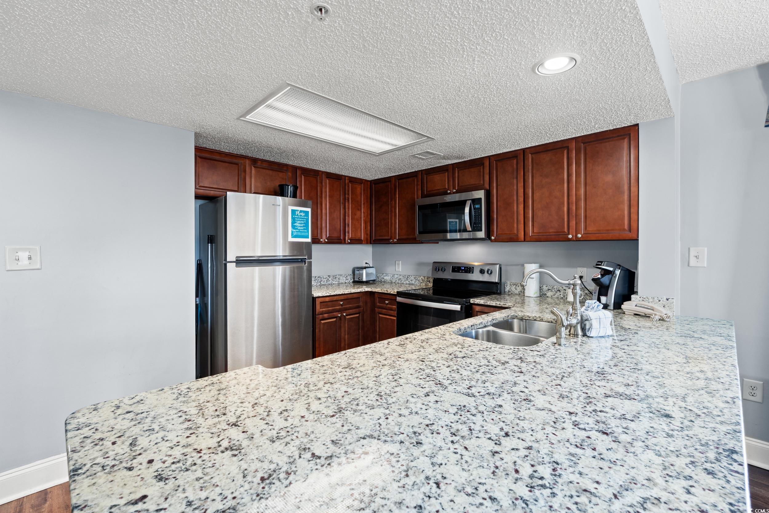 201N 74th Avenue North, Unit 601 Myrtle Beach, SC 29572 - Photo 6 of 35 Kitchen with stainless steel appliances, dark wood finished floors, light stone counters, a textured ceiling, and a peninsula