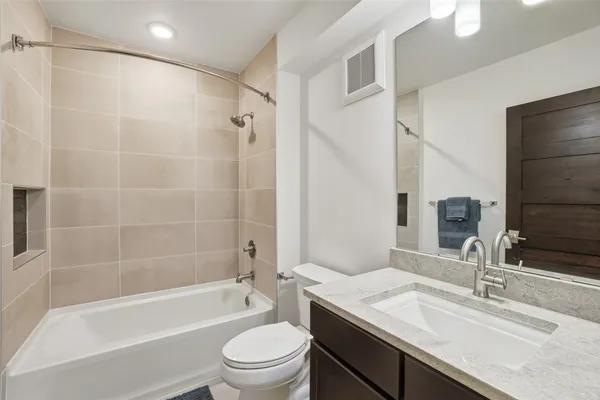 a bathroom with a granite countertop bathtub shower sink vanity mirror and toilet