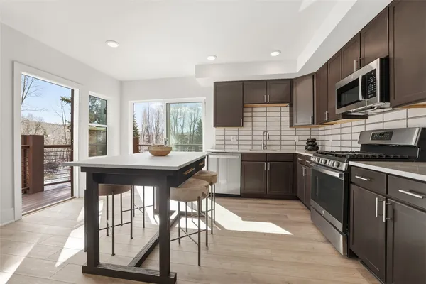 a kitchen with stainless steel appliances granite countertop a stove top oven a sink dishwasher a dining table and chairs with wooden floor