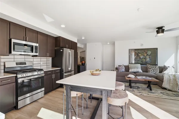 a kitchen with stainless steel appliances kitchen island granite countertop a stove top oven a sink dishwasher a dining table and chairs with wooden floor