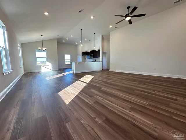 a view of an empty room and kitchen with wooden floor