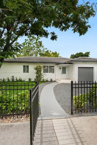 a view of house in front of a yard with potted plants and large trees