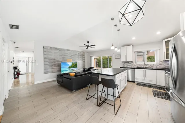 a kitchen with stainless steel appliances kitchen island granite countertop a refrigerator a stove a sink dishwasher and white cabinets with wooden floor
