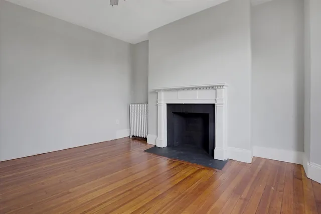 a view of an empty room with wooden floor and a fireplace