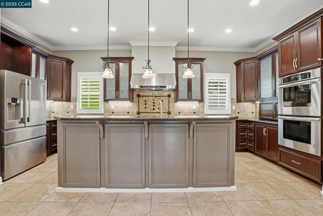 a kitchen with stainless steel appliances granite countertop a sink a stove a refrigerator and a wooden cabinets