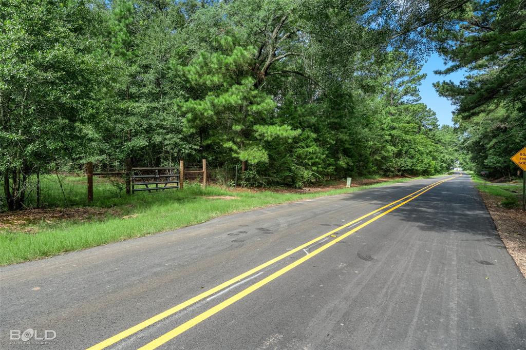 11015 Hereford Road Mooringsport, LA 71060 - Photo 10 of 18 Paved road frontage with double yellow lines, bordered by mature trees and a rustic wooden gate