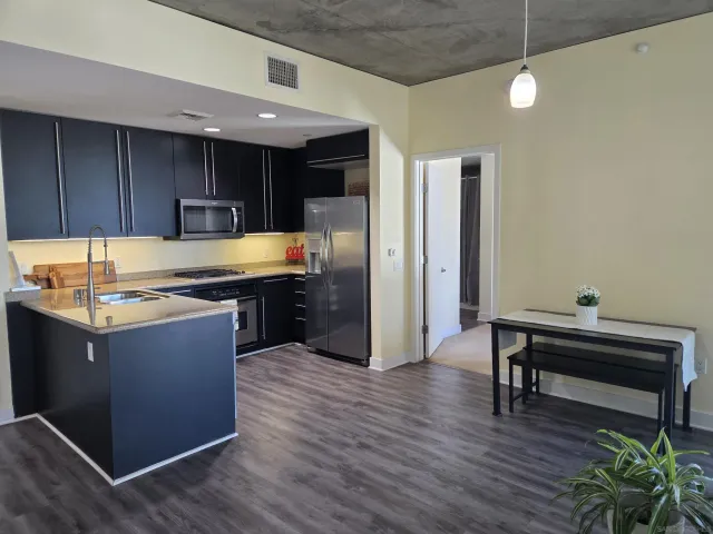 a kitchen with stainless steel appliances granite countertop a refrigerator a sink dishwasher a stove and a dining table with wooden floor