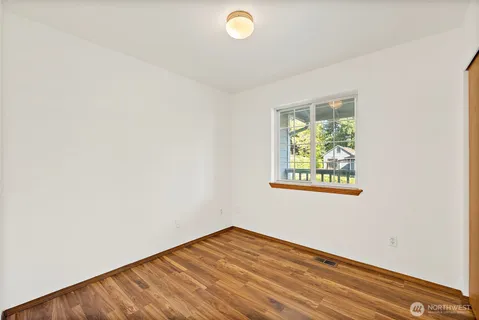 a view of an empty room with wooden floor and window