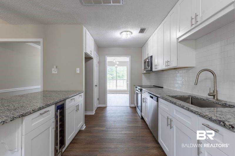 101 Lawson Road Daphne, AL 36526 - Photo 3 of 20 Renovated kitchen featuring wood-finish flooring, white shaker cabinetry, stainless steel appliances, and stone countertops