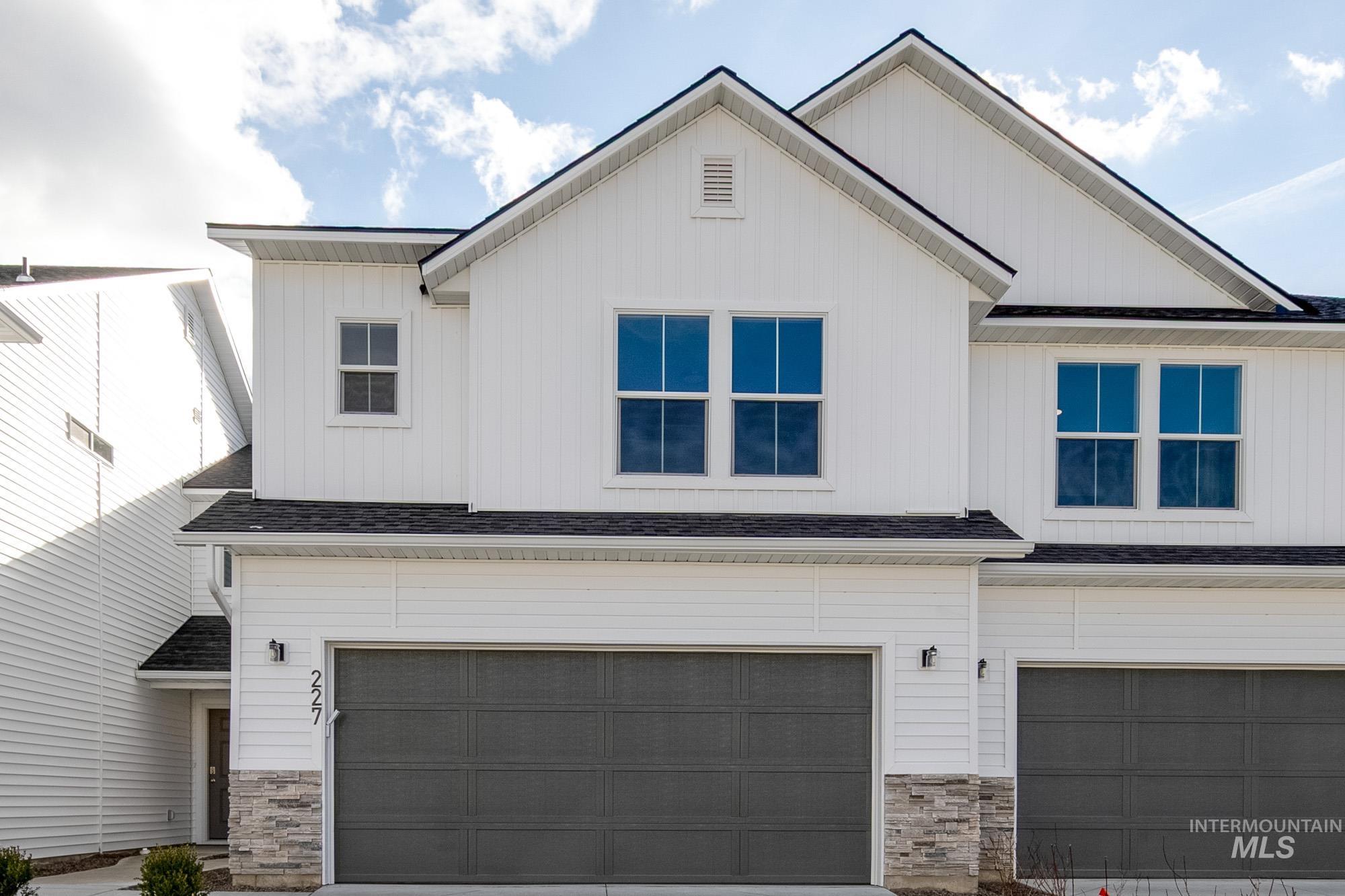 Modern inspired farmhouse featuring a garage, stone siding, board and batten siding, and a shingled roof