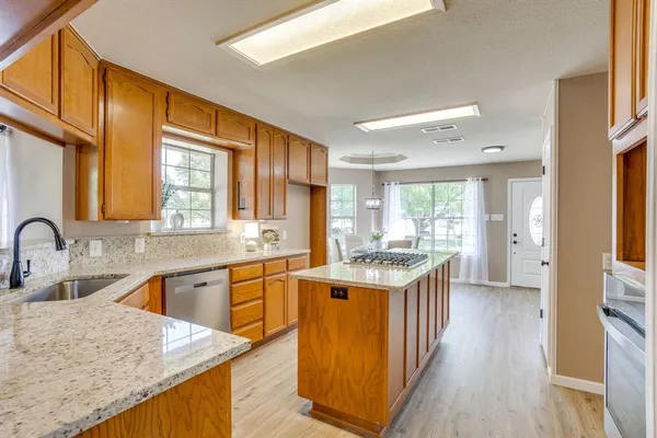 a kitchen with stainless steel appliances granite countertop wooden cabinets a sink dishwasher a stove and a refrigerator