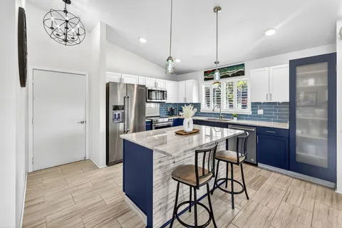 a kitchen with stainless steel appliances kitchen island granite countertop a refrigerator a stove a sink dishwasher and a dining table with wooden floor
