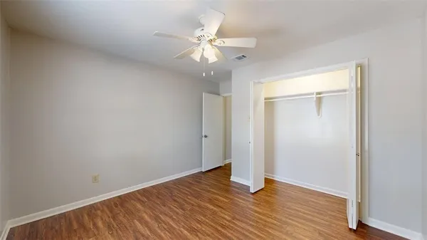 an empty room with wooden floor fan and windows