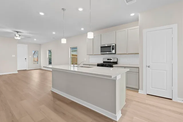 a open kitchen with kitchen island a sink dishwasher a refrigerator and white cabinets with wooden floor
