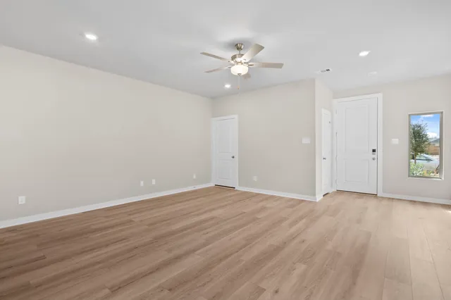 a view of an empty room with wooden floor and a ceiling fan