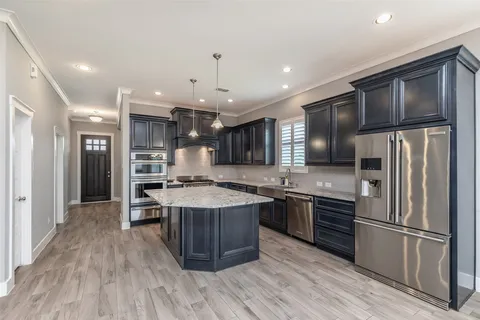 a kitchen with stainless steel appliances granite countertop a stove top oven a refrigerator a sink and a dining table with wooden floor