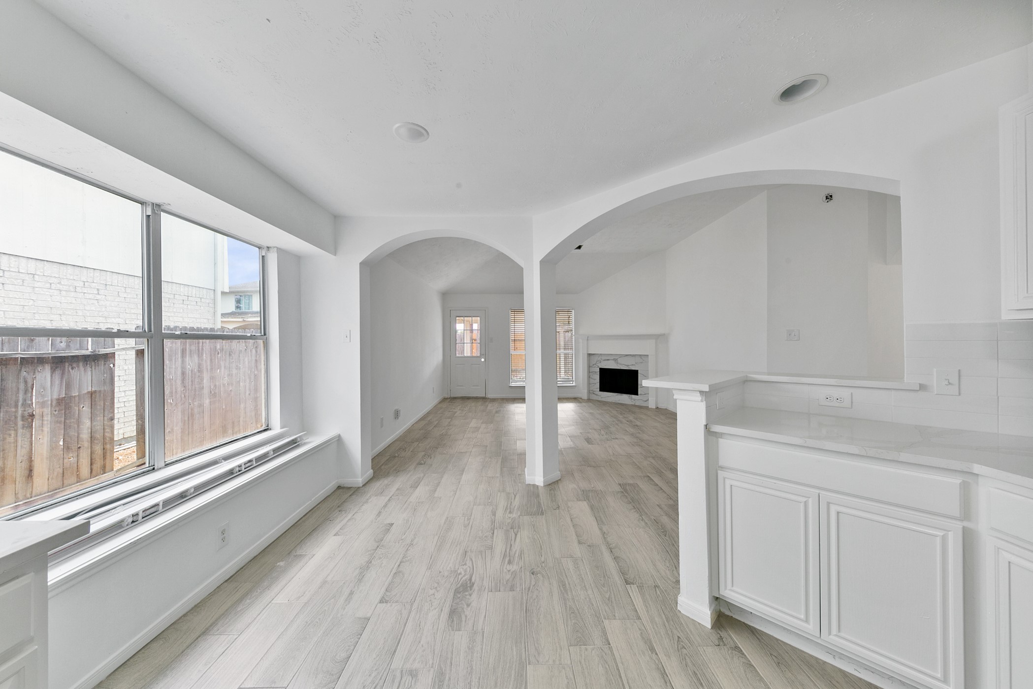 12014 Raven View Drive Houston, TX 77067 - Photo 18 of 29 Bright and open living space featuring large windows, light wood flooring, and a cozy fireplace. The arched doorway leads to a well-lit area, perfect for entertaining. The kitchen area includes sleek white cabinetry and a breakfast bar.