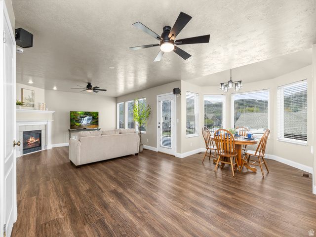 6849 North Black Powder Road Mountain Green, UT 84050 - Photo 4 of 43 Spacious living area featuring wood-finish flooring, a fireplace with a white mantle, ceiling fans, and a dining nook with bay windows