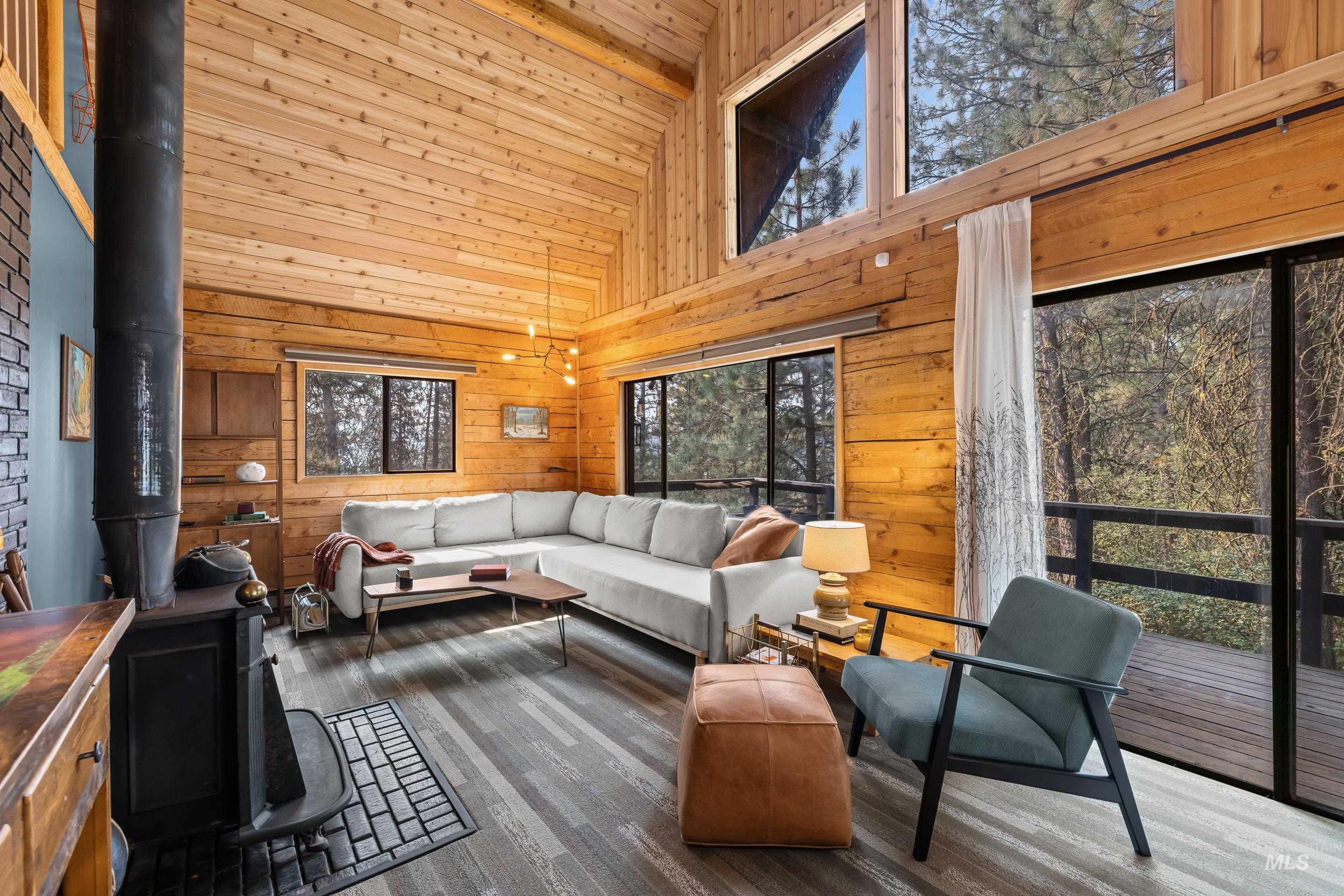 73 Rainbow Ridge Road Garden Valley, ID 83622 - Photo 23 of 49 Vaulted wood plank ceilings, wood-finish flooring, exposed wood beam construction, and a black wood-burning stove with a brick hearth