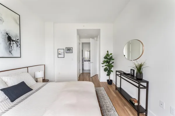 a bedroom with a bed a mirror and a potted plant on the dresser