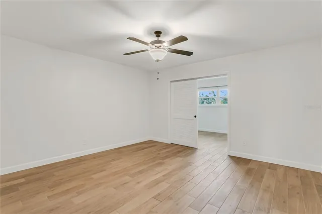 an empty room with wooden floor ceiling fan and window