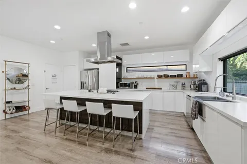 a large kitchen with stainless steel appliances a stove a refrigerator a oven a sink with a dining table and chairs with wooden floor