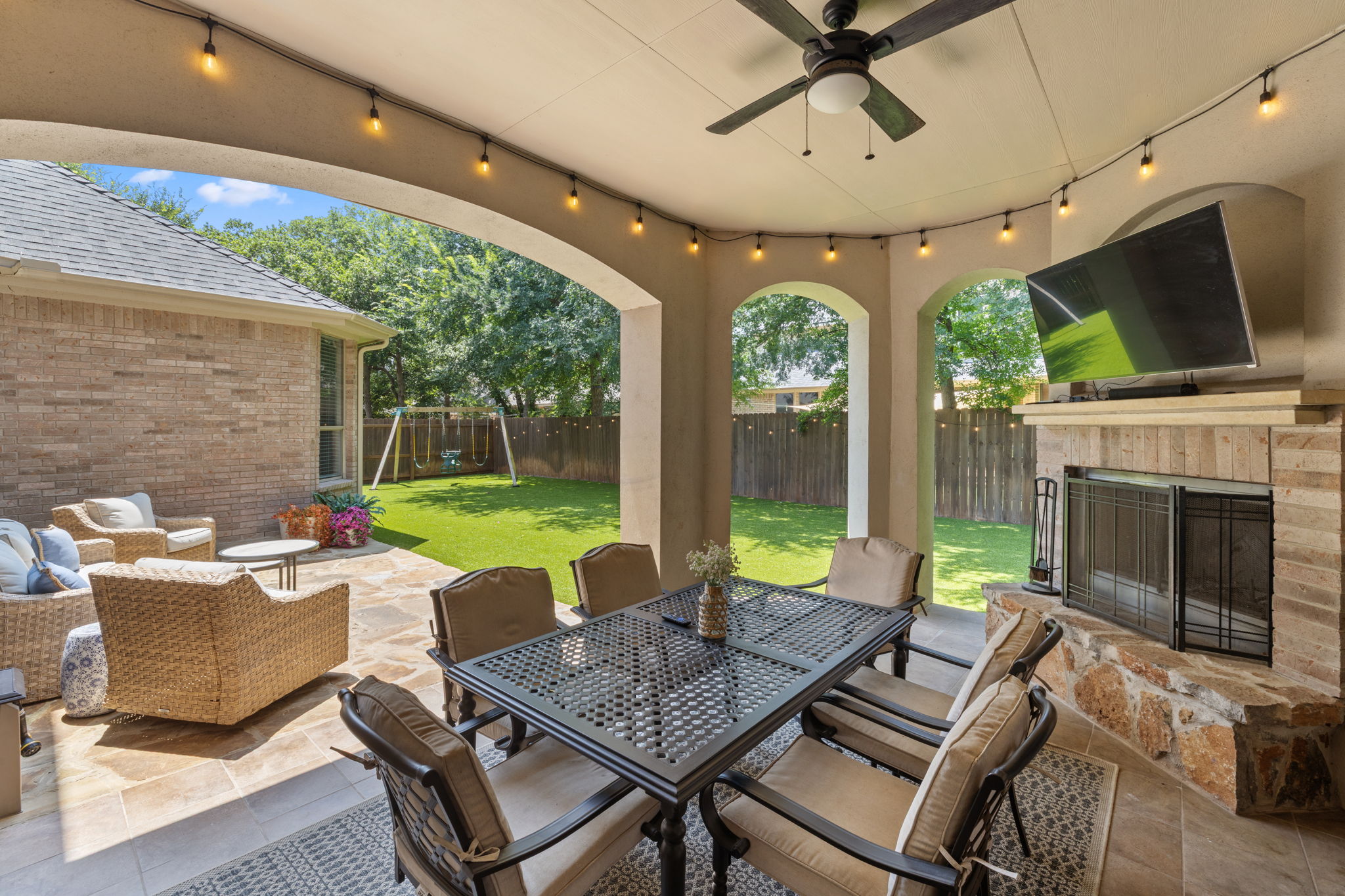 1124 Castle Path Round Rock, TX 78681 - Photo 36 of 40 An inviting covered patio featuring a dining area, ceiling fan, and stone fireplace, opening to a private green yard.